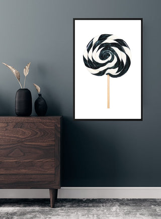 Poster of a black and white swirling lollipop hanging on a dark wall above a wooden chest in a modern room.