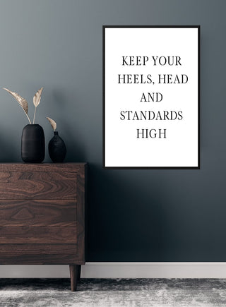 Minimalist poster on a wall reads "Keep your heels, head and standards high" above a wooden dresser.
