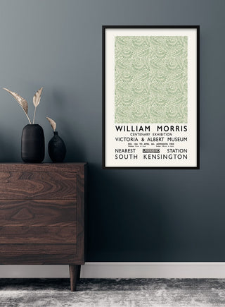 Framed William Morris green poster with intricate pattern hanging on a dark wall above a wooden dresser.