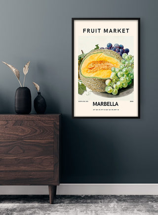Poster of a cantaloupe and grapes with "Fruit Market Marbella" text, framed on a modern living room wall.