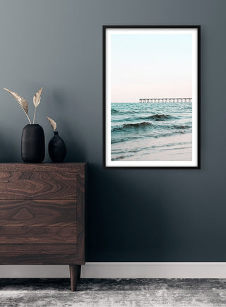 Framed Long Bridge by the Sea Plakat hanging on a dark wall above a wooden dresser in a modern room.