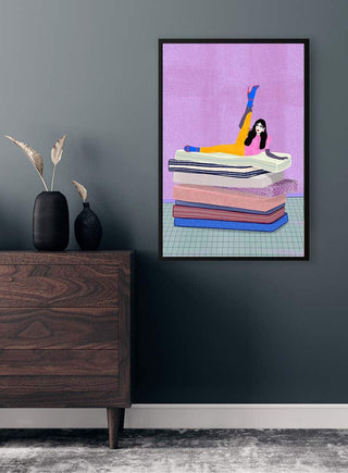 Framed art print of a woman raising her leg up on stacked books, displayed above a wooden dresser.