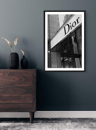 Framed black and white Dior storefront photo displayed above a wooden dresser in a modern room.