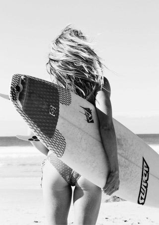 Woman in swimwear holding a surfboard on the beach, showcasing Surfers Fashion’s coastal style.