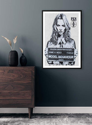 Framed Kate Moss street art poster on a gray wall above a wooden dresser in a modern room.