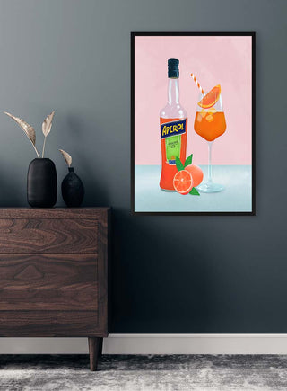 Framed image of Aperol bottle and spritz cocktail with orange slice, displayed above a modern wooden dresser.