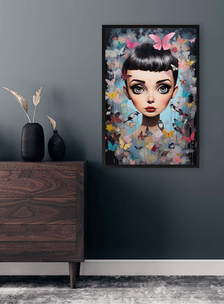 Framed “Young Audrey Hepburn - Tara Green” portrait with butterfly motifs hung on a dark wall above a wooden dresser.