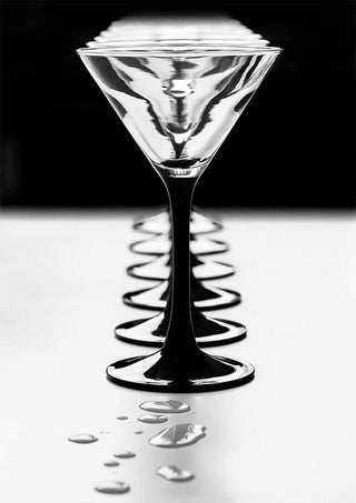 A line of elegant Giorgio Toniolo goblets with reflections and water droplets on a smooth surface.
