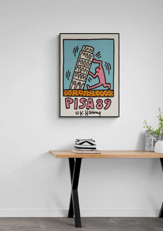 Framed Pisa - Keith Haring artwork featuring a figure with the Leaning Tower of Pisa on a modern wall above a table.