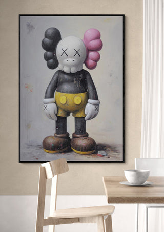 Framed Kaws Classic - Danii Steinfeldt artwork displayed on a beige wall above a wooden chair and table.