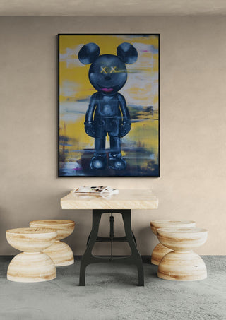 Framed artwork "Kawsey" by Daniel Leo hangs above a wooden table with three round stools in a modern room.