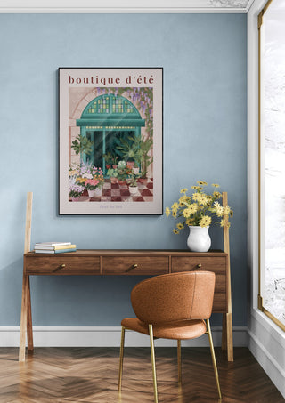 Cozy workspace with flowers, wooden desk, and framed French floral shop print on a soft blue wall.