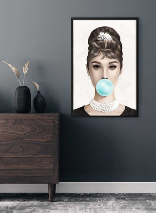 Poster of Audrey Hepburn blowing bubblegum, hanging on a dark wall above a modern wooden dresser.