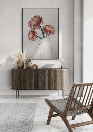 Artwork "In Bloom" by Gabriella Roberg featuring red flowers in a white vase, displayed above a wooden sideboard.