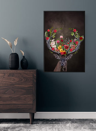 Poster of a deer with antlers adorned with colorful flowers, hanging on a dark wall above a wooden dresser.