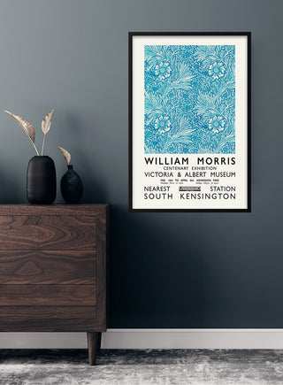 Framed William Morris blue poster featuring floral patterns, displayed on a dark wall above a wooden dresser.