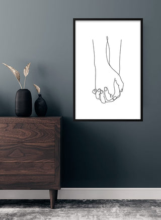 Minimalist art print of two hands holding each other, framed and hung on a dark wall above a wooden dresser.