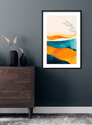 Framed Japanese cranes art print with abstract orange and blue waves hanging above a dark wood dresser.