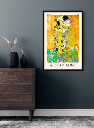 Framed Gustav Klimt - The Kiss poster hanging on a dark wall above a wooden dresser with a vase.