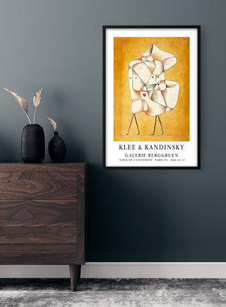 Framed Klee & Kandinsky Exhibition Plakat on a gray wall above a wooden dresser with vase and dried plants.