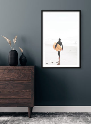 Framed poster of a surfer walking on the beach, carrying a surfboard, displayed above a wooden dresser.
