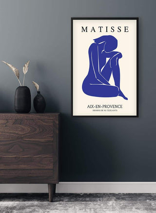 Framed Matisse inspired blue cutout poster of a seated figure, displayed on a wall above a modern dresser.