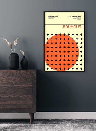 Framed Bauhaus Orange & Stars Weimar Plakat on a dark wall above a wooden dresser with minimalist decor.