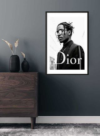 Framed Asap Rocky x Dior poster hanging on a gray wall above a dark wooden dresser.