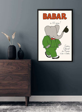 Framed Babar Plakat No. 04 featuring Babar the elephant in a green suit, displayed on a grey wall above a dresser.