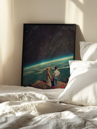 Framed "Love" by Frank Moth print showing a couple holding hands, gazing at Earth from space, on a sunlit bed.