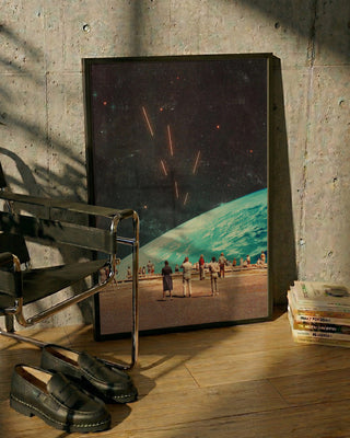 Framed print of "The Others" by Frank Moth resting on the floor beside a chair, shoes, and stacked books.