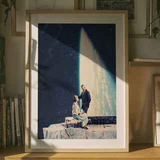 Framed print of “This Love” by Frank Moth showing a couple on a cliff with a cosmic background, displayed on a shelf.
