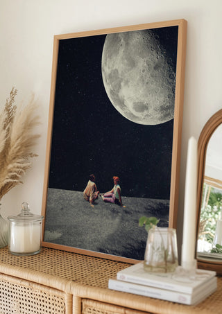 Framed art print of two people sitting together under a large moon, by Frank Moth, displayed on a wooden shelf.