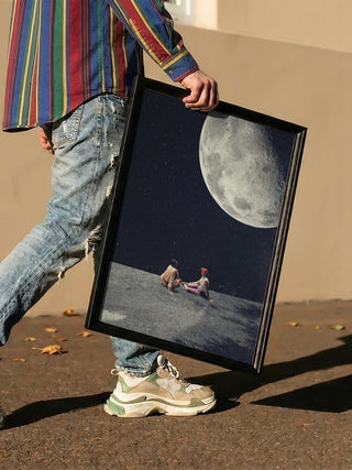 Person holding framed "I Gave You the Moon for a Smile" artwork by Frank Moth, depicting two figures under a large moon.