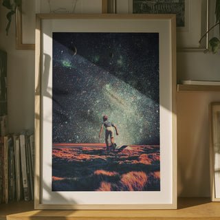 Framed art print of a lone astronaut on an orange landscape under a star-filled cosmic sky, displayed indoors.