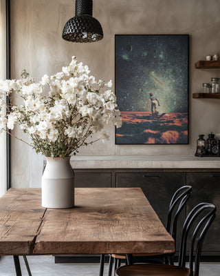 Nostalgia print by Frank Moth on wall above rustic dining table with vase of white flowers in cozy kitchen.