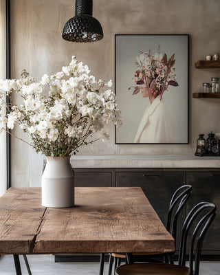 Dining room with wooden table, vase of white flowers, and "I Fell In Love With Fall Because of You" by Frank Moth on wall.