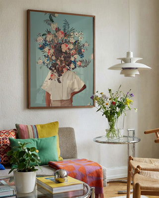 Framed "Thank God It's Spring" by Frank Moth hanging above a cozy, colorful living room with flowers.