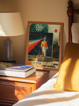 Framed "You Can Make It Right" by Frank Moth on bedside table next to lamp, books, and bed with yellow pillow.