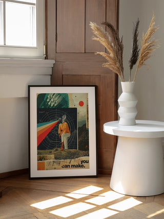 Framed "You Can Make It Right" art print by Frank Moth leaning on a wall beside a white round table with vase.