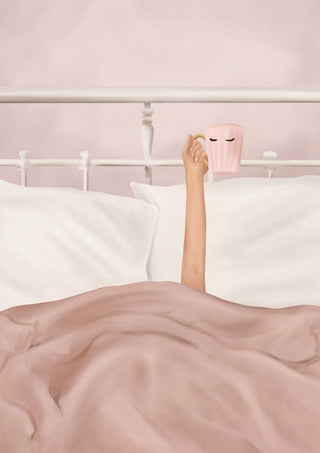 A person in bed lifts a pink Flow Line coffee cup with eyes design, surrounded by soft bedding.