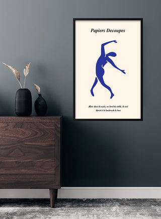 Minimalist blue dancer poster in Matisse style, framed and hung on a dark wall above a wooden dresser.