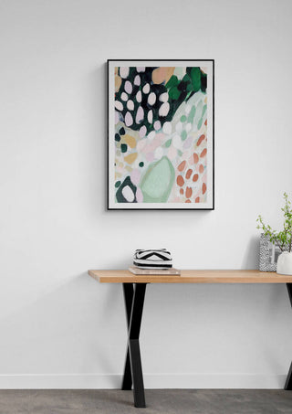 Abstract Rose Garden artwork in black frame displayed above a modern wooden table with decorative items.