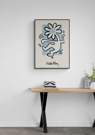 Poster of Keith Haring's Flowerhead artwork hanging above a wooden table with minimalist decor.