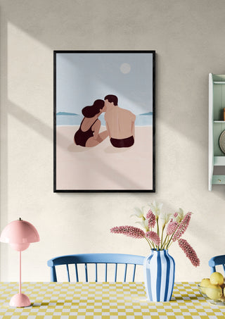 Framed art of a couple sharing a first kiss on the beach, displayed above a dining table with flowers.