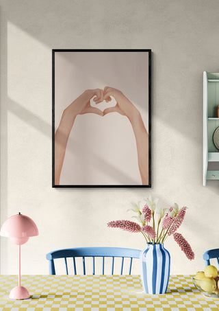 Framed artwork of hands forming a heart shape, displayed above a dining table with flowers and pastel decor.