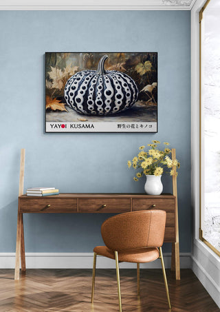 Framed Yayoi Kusama Black Pumpkin artwork hanging above a wooden desk with flowers in a modern room.