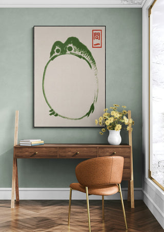 Framed Grumpy Toad III - Matsumoto Hoji print hanging above a wooden desk with flowers in a vase.