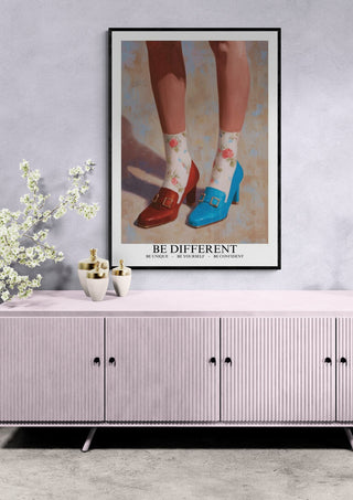 Framed "Be Different Louboutin - Martina Karlsson" poster above a light pink cabinet in a modern room.