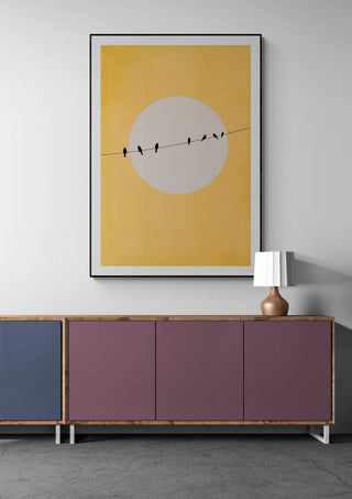 Chirping and Chilling - Boris Draschoff artwork of birds on a wire against a yellow sun, framed above modern credenza.